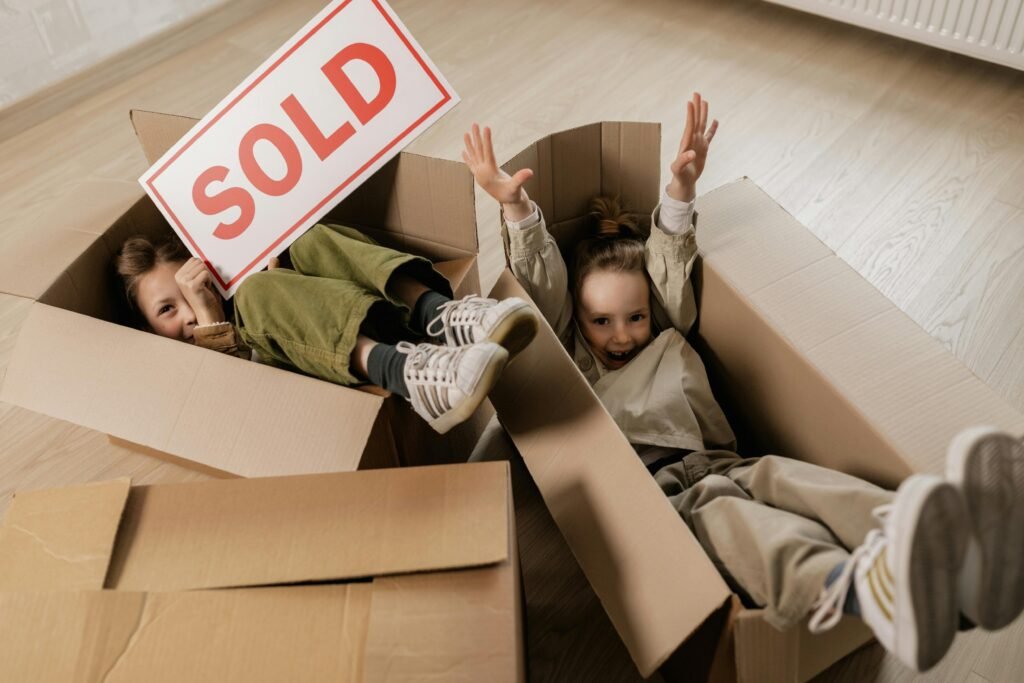 Two happy children playing with cardboard boxes indoors, celebrating moving to a new home.